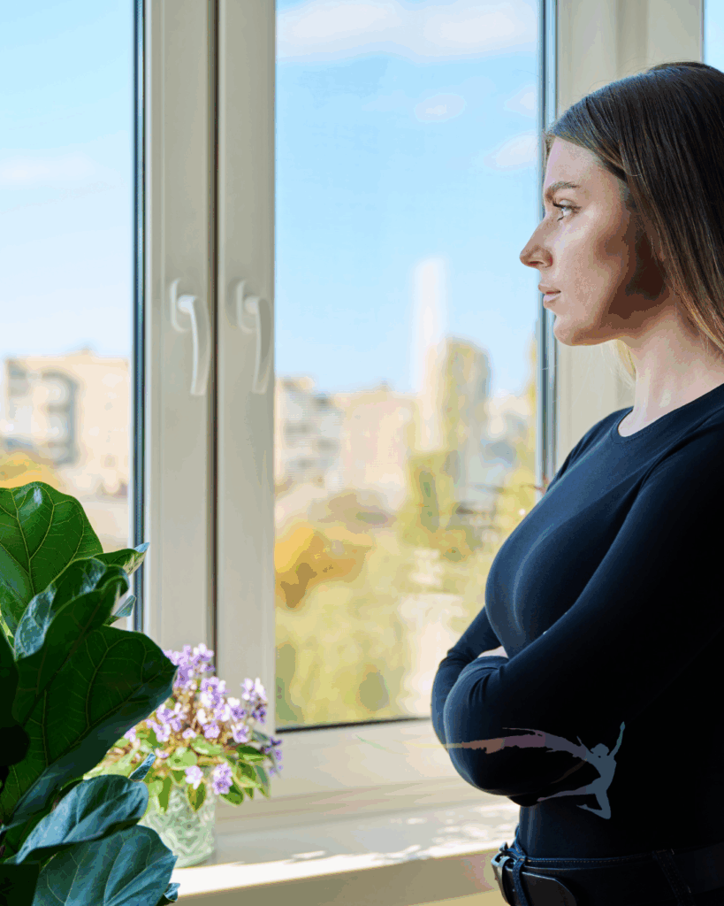 vrouw kijkt nadenkend uit het raam – symbool voor onrust, verandering en zelfreflectie
